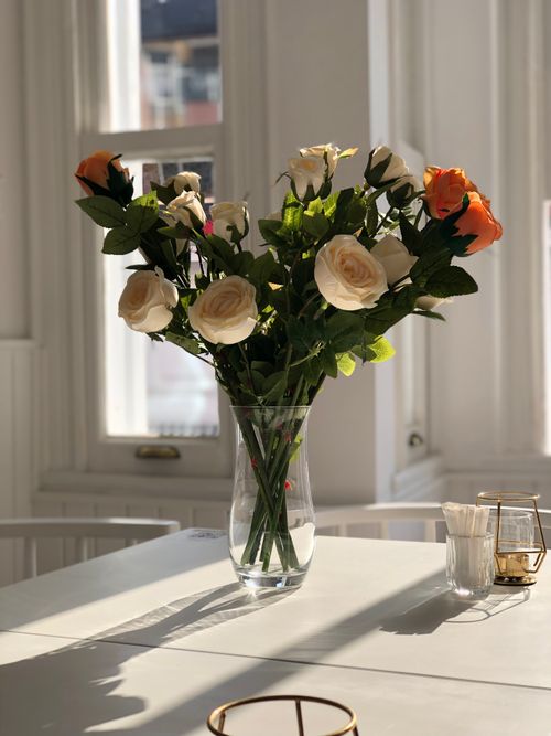 Free Beautiful bouquet of roses in a glass vase on a sunlit white table indoors. Stock Photo