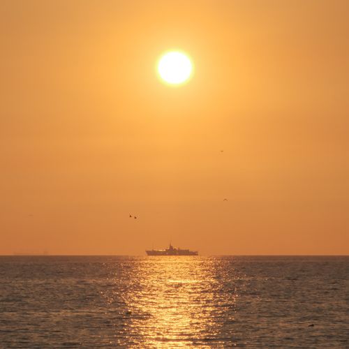 Free A serene golden sunset over the sea with a distant ship silhouette reflecting on the water. Stock Photo