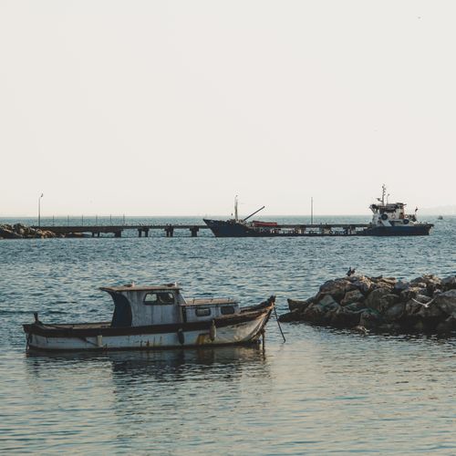 Free Peaceful seaside view featuring fishing boats and a rocky pier under a clear sky. Stock Photo