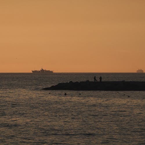 Silhouetted Breakwater and Ships on the Horizon at Sunset 