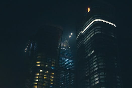 A dramatic nighttime cityscape featuring illuminated skyscrapers against a dark sky.
