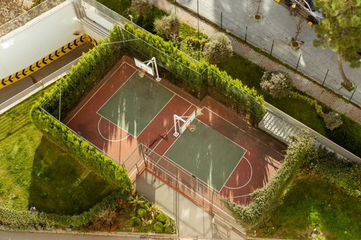 Top-down view of a secluded basketball court surrounded by lush greenery in an urban setting.