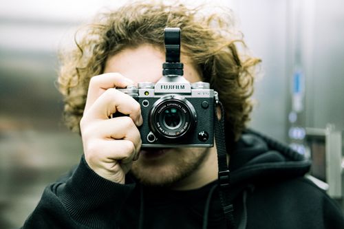 Free Close-up portrait of a photographer holding a Fujifilm camera, capturing the moment in an urban setting. Stock Photo