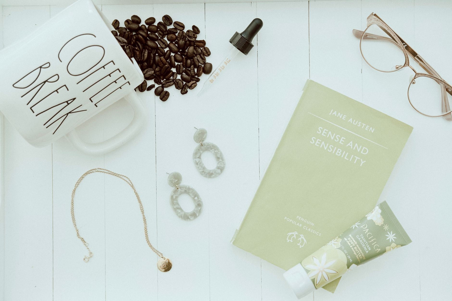 Aesthetic flat lay featuring coffee, book, jewelry, and skincare.