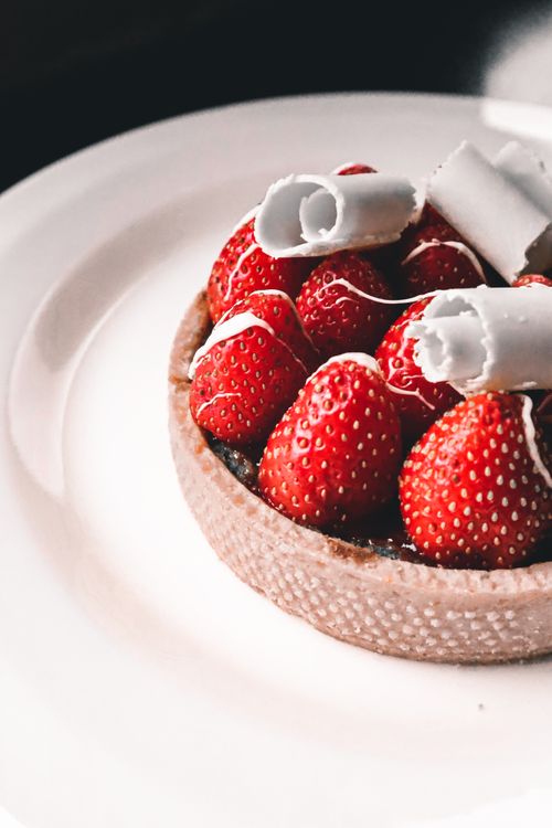 Free Close-up of a fresh strawberry tart topped with white chocolate curls on a white plate. Stock Photo