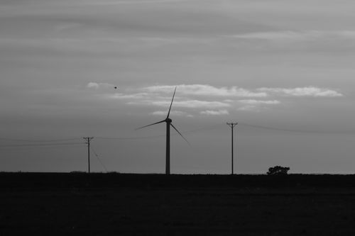 Free Black and white image of a wind turbine and power lines in a rural landscape, symbolizing clean energy. Stock Photo