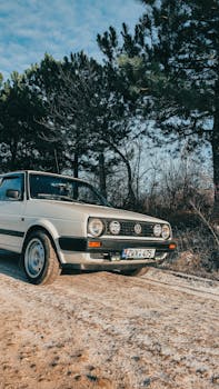 Vintage Volkswagen car parked on a sunlit dirt road surrounded by trees.