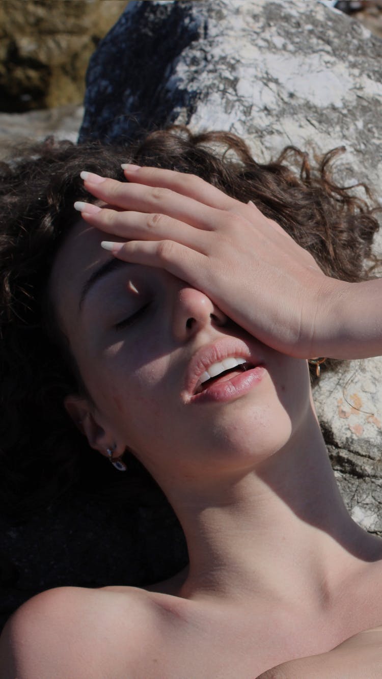 A Woman Lying On Rock Covering Her Eye With Hand