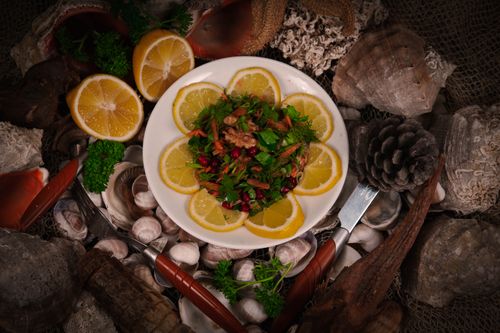 Free Colorful salad with lemon slices and nuts on a plate, surrounded by seashells and pine cones, creating a natural aesthetic. Stock Photo