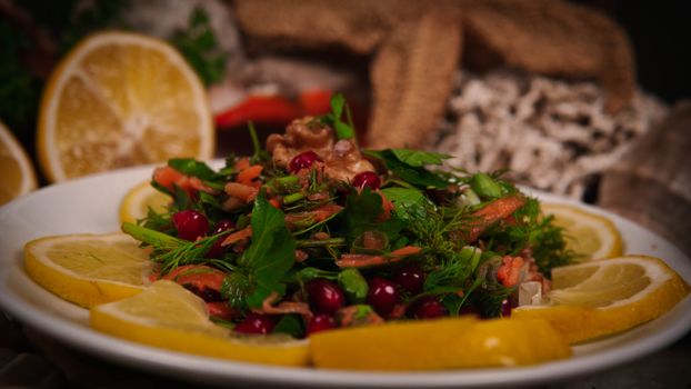 Vibrant mixed salad with fresh herbs, lemon slices, and walnuts on a white plate.