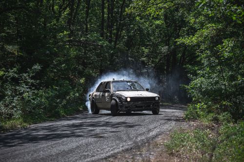 Free A classic car drifting on an asphalt road surrounded by dense green forest. Stock Photo