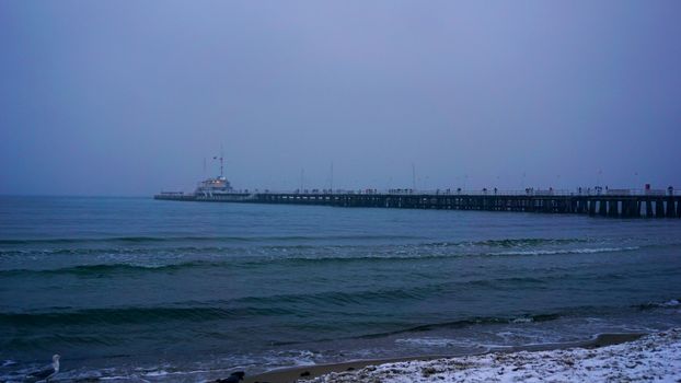 Capture of Sopot Pier with gentle waves under a moody winter twilight sky.