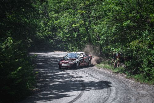 Free Experience the adrenaline of a rally car drifting around a gravel track in a lush forest setting. Stock Photo