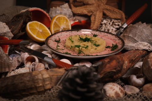 Free A gourmet dish garnished with dill, surrounded by seashells and sliced lemons in a rustic setting. Stock Photo