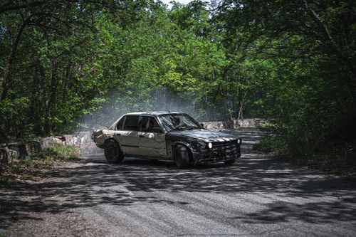 Free Vintage car drifting on a secluded forest road, surrounded by lush, green trees. Stock Photo