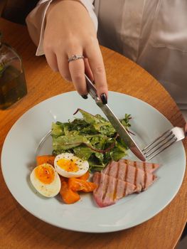 Cutting a balanced meal of salad, boiled egg, and tuna on a table.