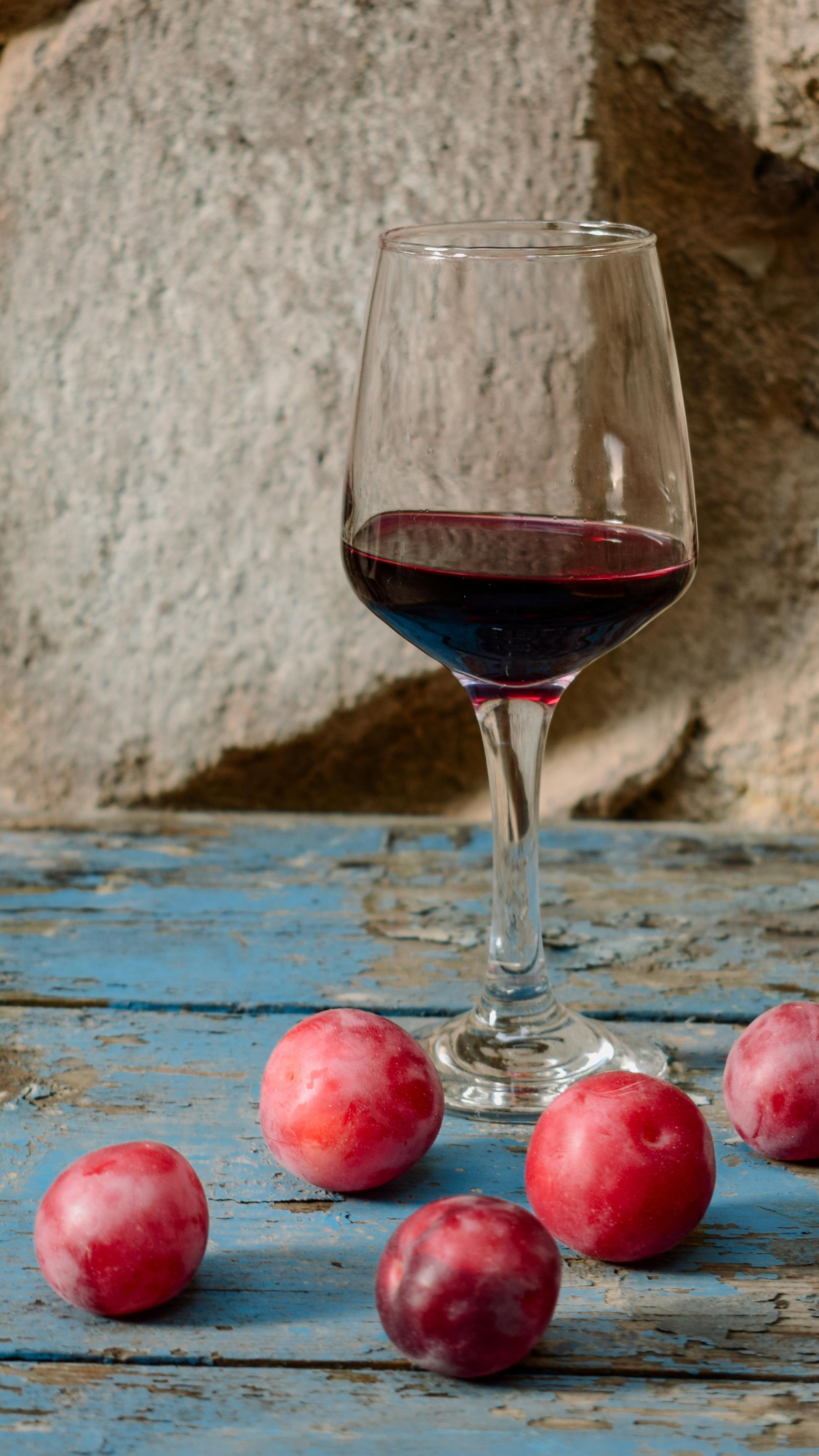 a glass of red wine and some plums on a blue table