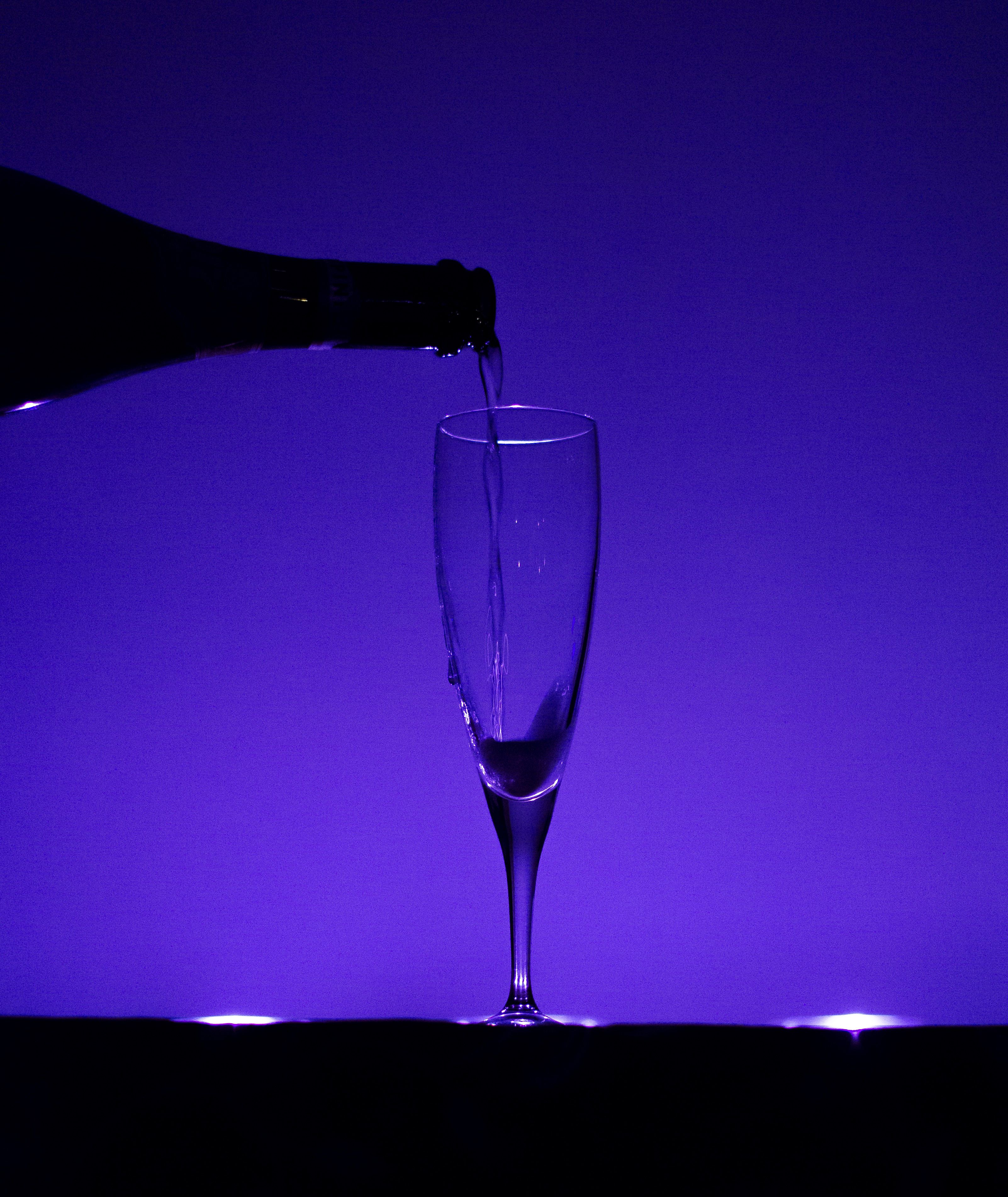 Elegant silhouette of champagne being poured into a glass against a purple backdrop.