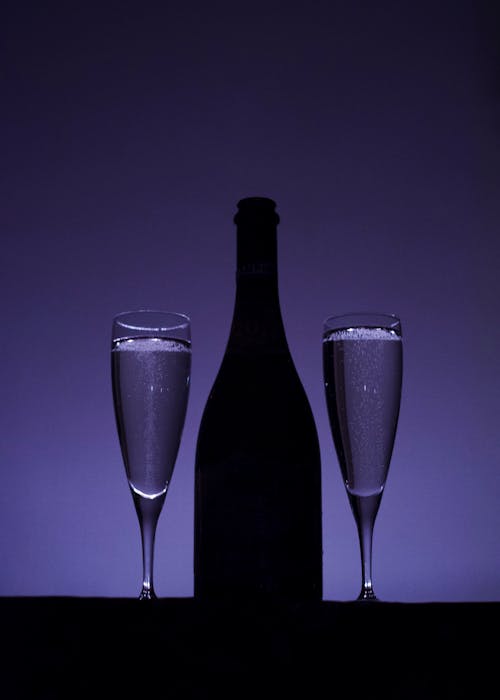 A Silhouette of a Bottle of Champagne beside Champagne Glasses