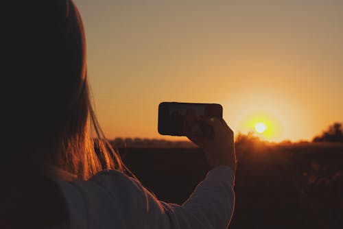 Silhouette Photo of Woman Taking Photo of Sunset