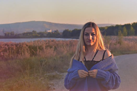 日落时分，一位穿着蓝色毛衣的女子站在湖边，四周被大自然环绕