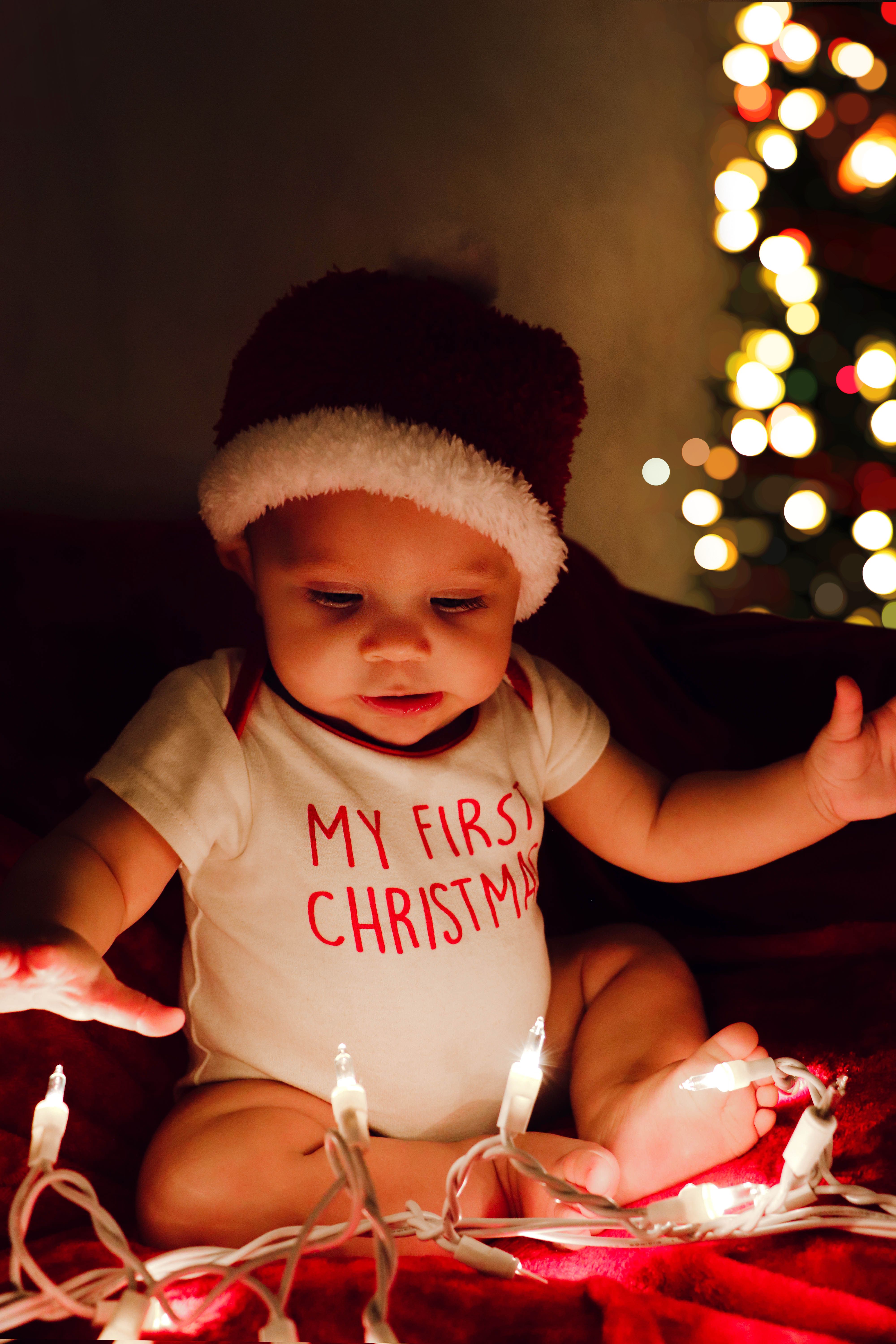 Cute baby in Santa hat playing with festive lights, celebrating first Christmas.