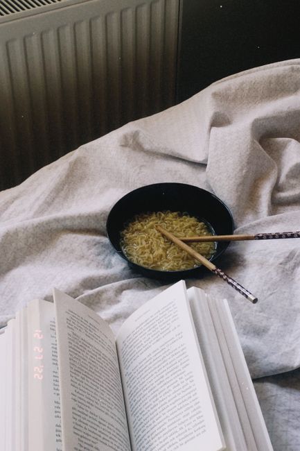 A warm indoor setup featuring a bowl of noodles and an open book on a cozy blanket.