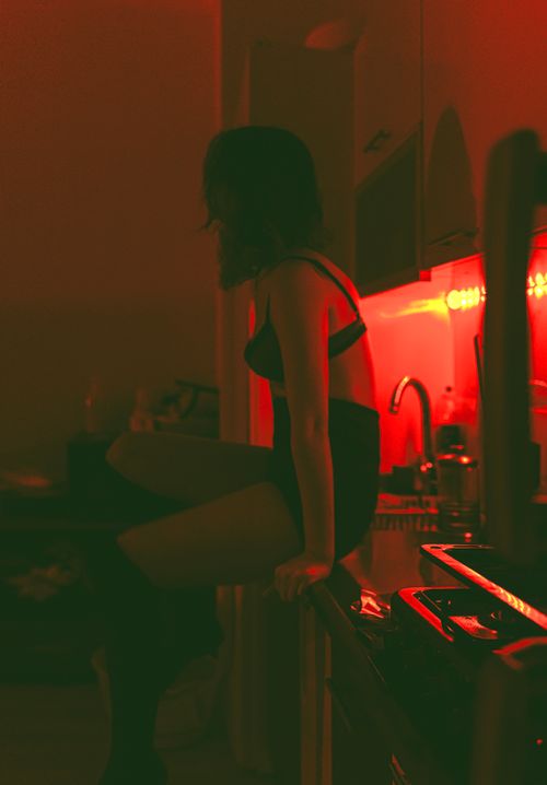 Free Silhouette of a woman sitting in a dimly lit room with dramatic red lighting. Stock Photo