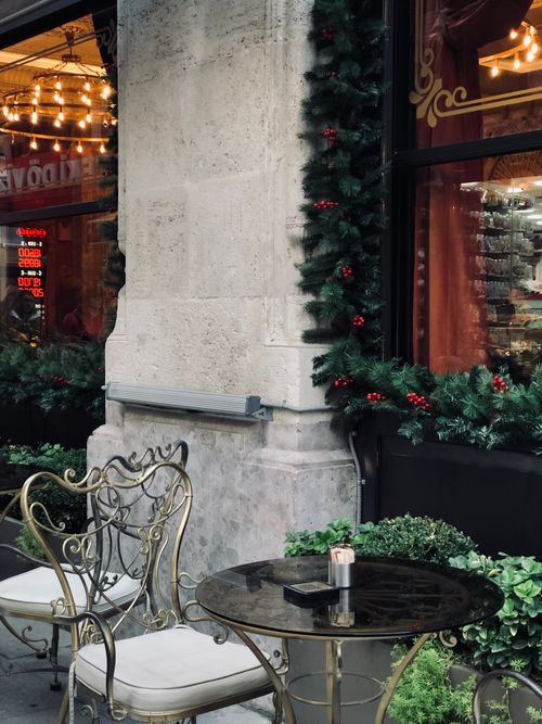 Free Charming outdoor café table with festive garland decor and elegant chairs, evoking a cozy holiday atmosphere. Stock Photo