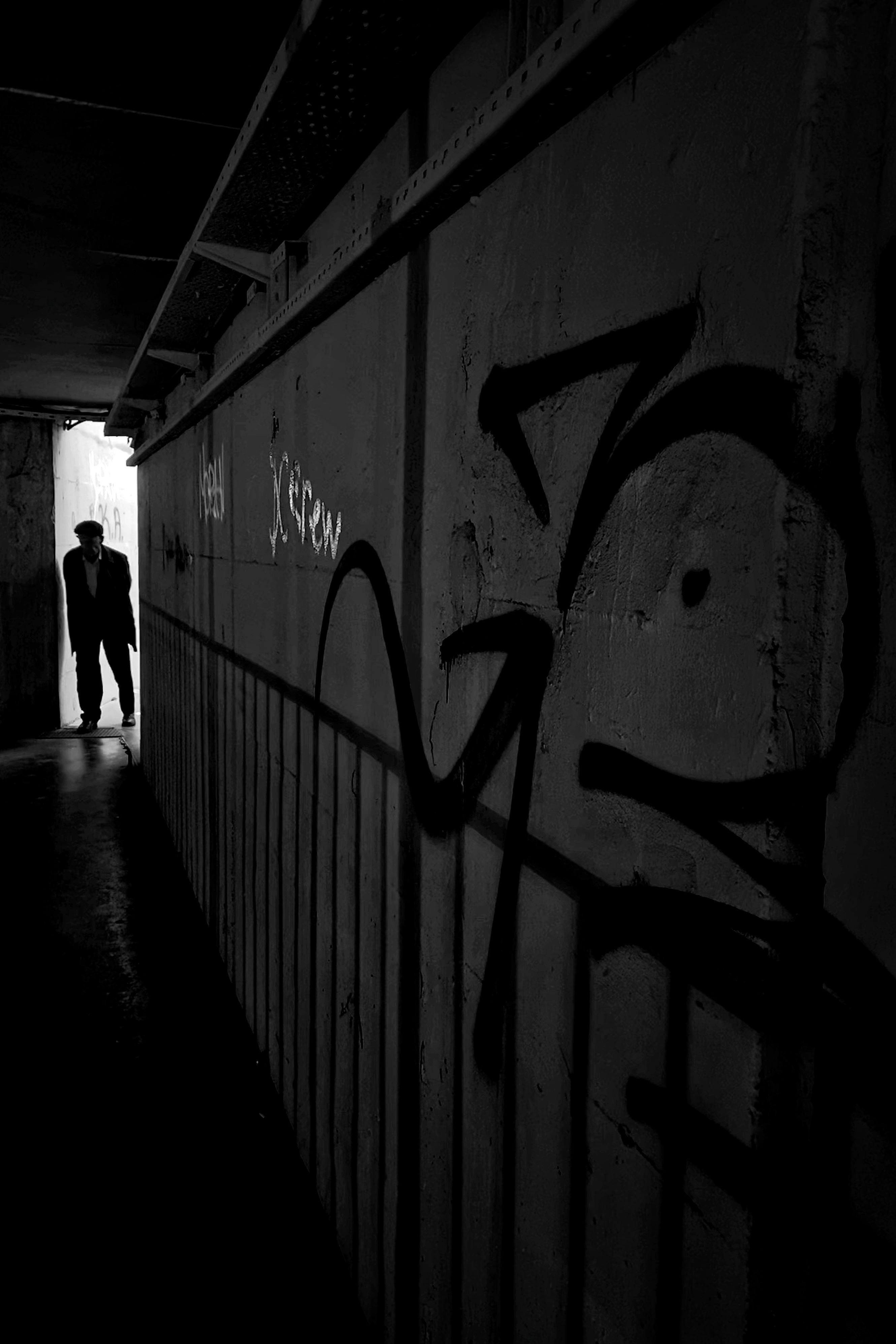 Mysterious silhouette in narrow corridor with dramatic graffiti and contrasting shadows.