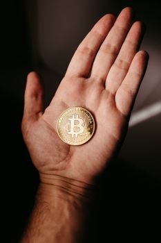 Close-up of a hand holding a gold Bitcoin, highlighting the digital currency concept.