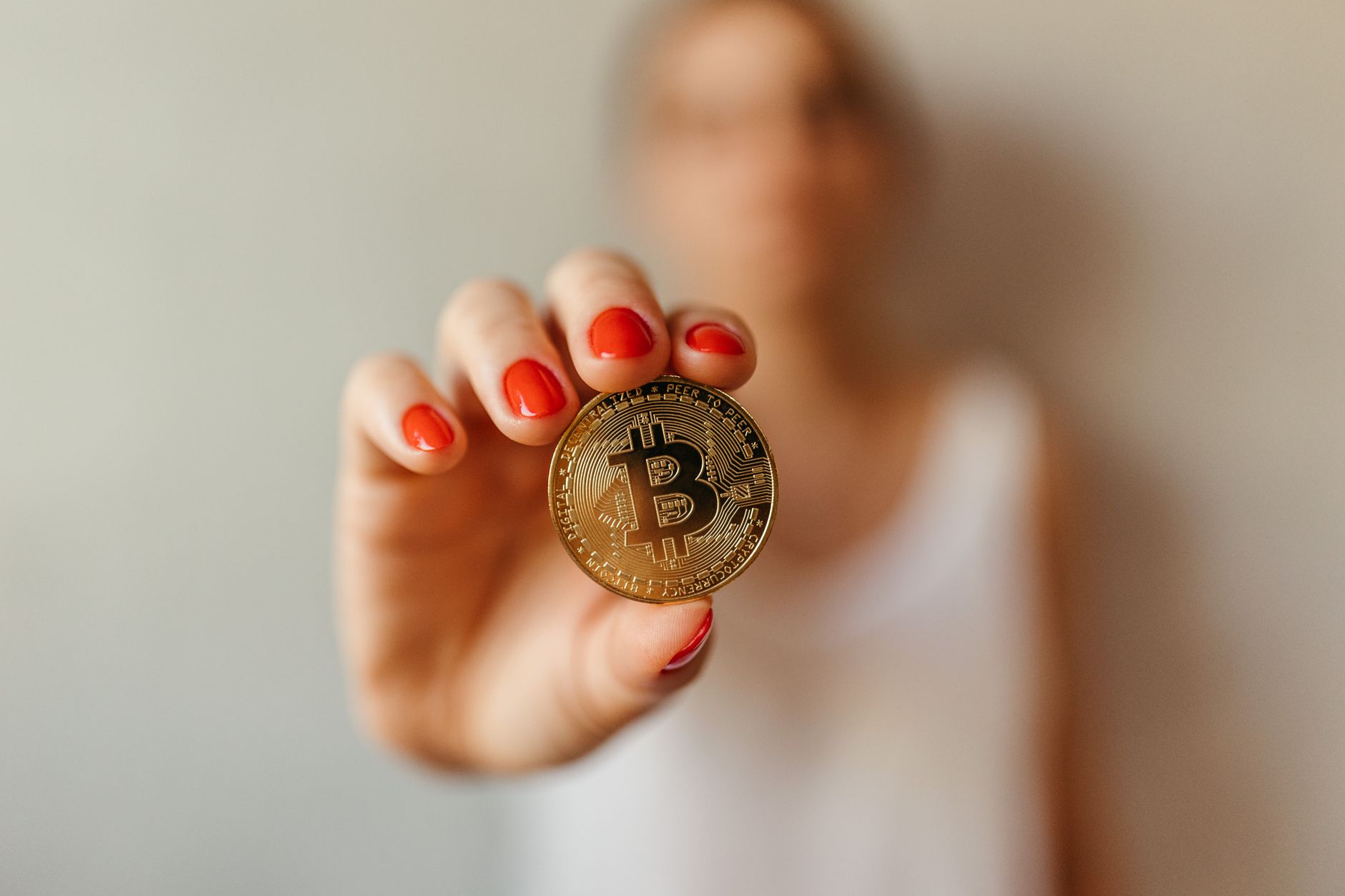 Focused shot of a Bitcoin coin held by a person with red nails, symbolizing digital currency.
