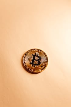 Close-up of a golden Bitcoin on a neutral surface, highlighting cryptocurrency symbolism.