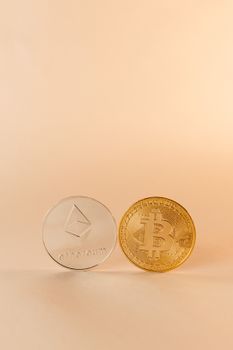 Gold Bitcoin and silver Ethereum coins displayed against a solid neutral background, symbolizing cryptocurrency.