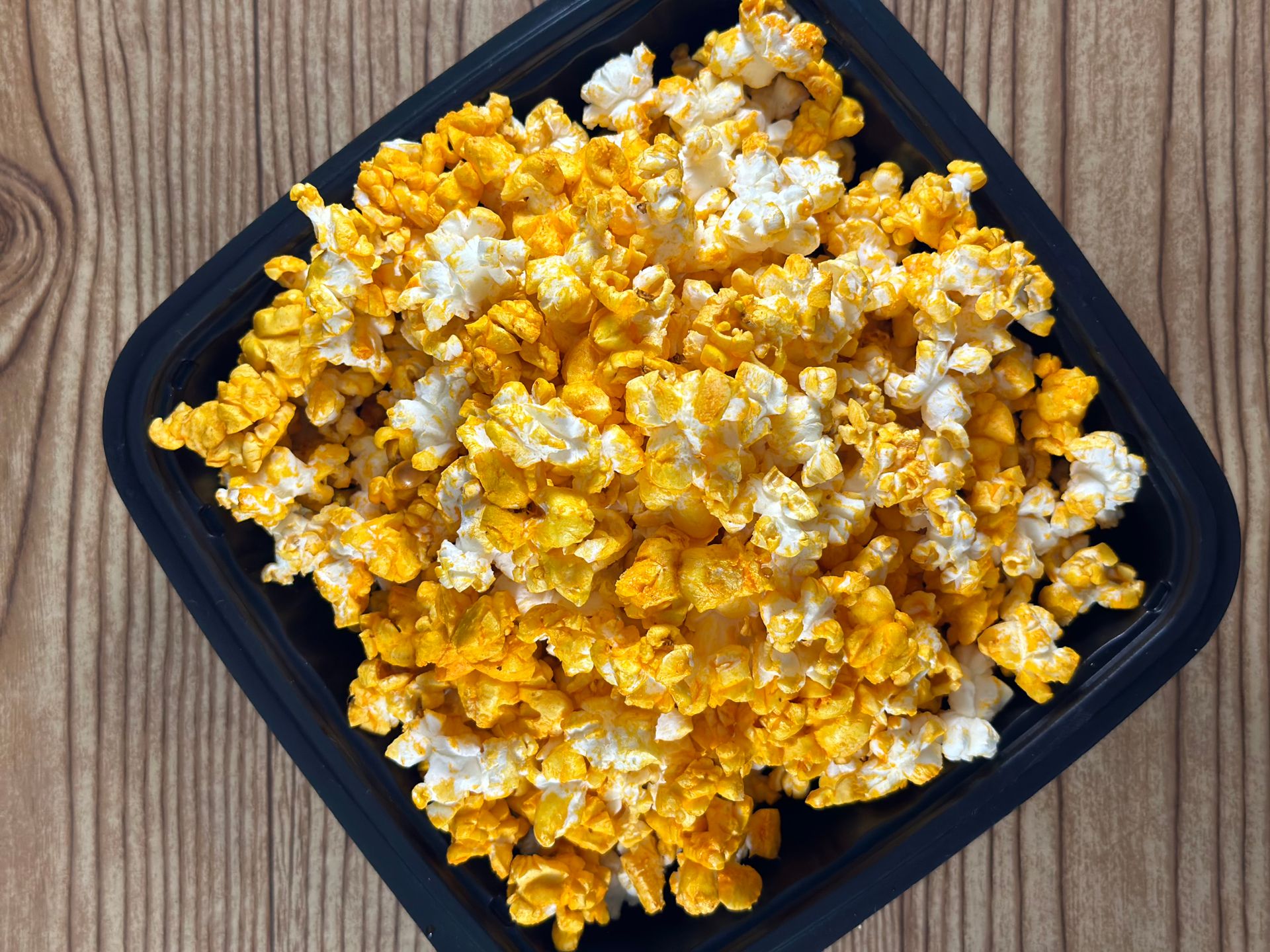 Overhead view of cheddar popcorn in a black bowl on a wooden table. Perfect snack shot.