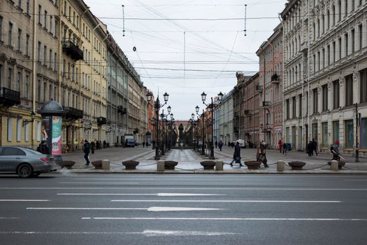 A bustling urban street scene in a historic European city with pedestrians and parked cars.
