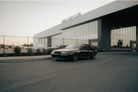 Sleek black sports car parked outside Million Air private jet terminal during daytime.