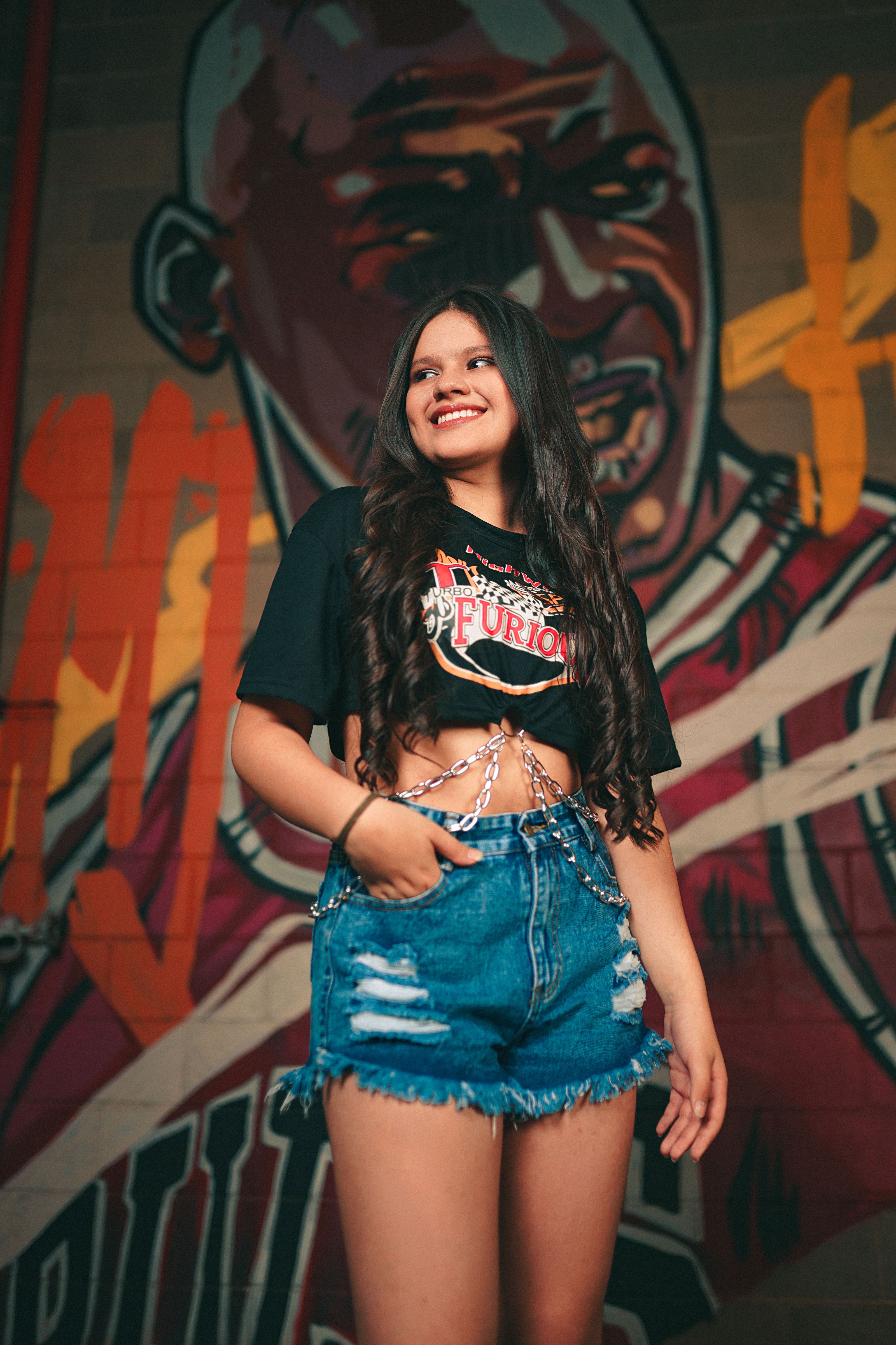 Jovem mulher estilosa posando em frente a um mural de arte urbana.