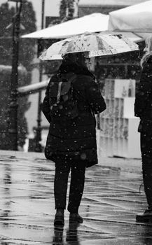 A woman walks outdoors in the rain, holding an umbrella, captured in black and white.