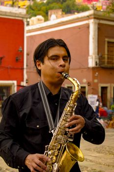 A young man skillfully playing the saxophone in a vibrant outdoor setting.