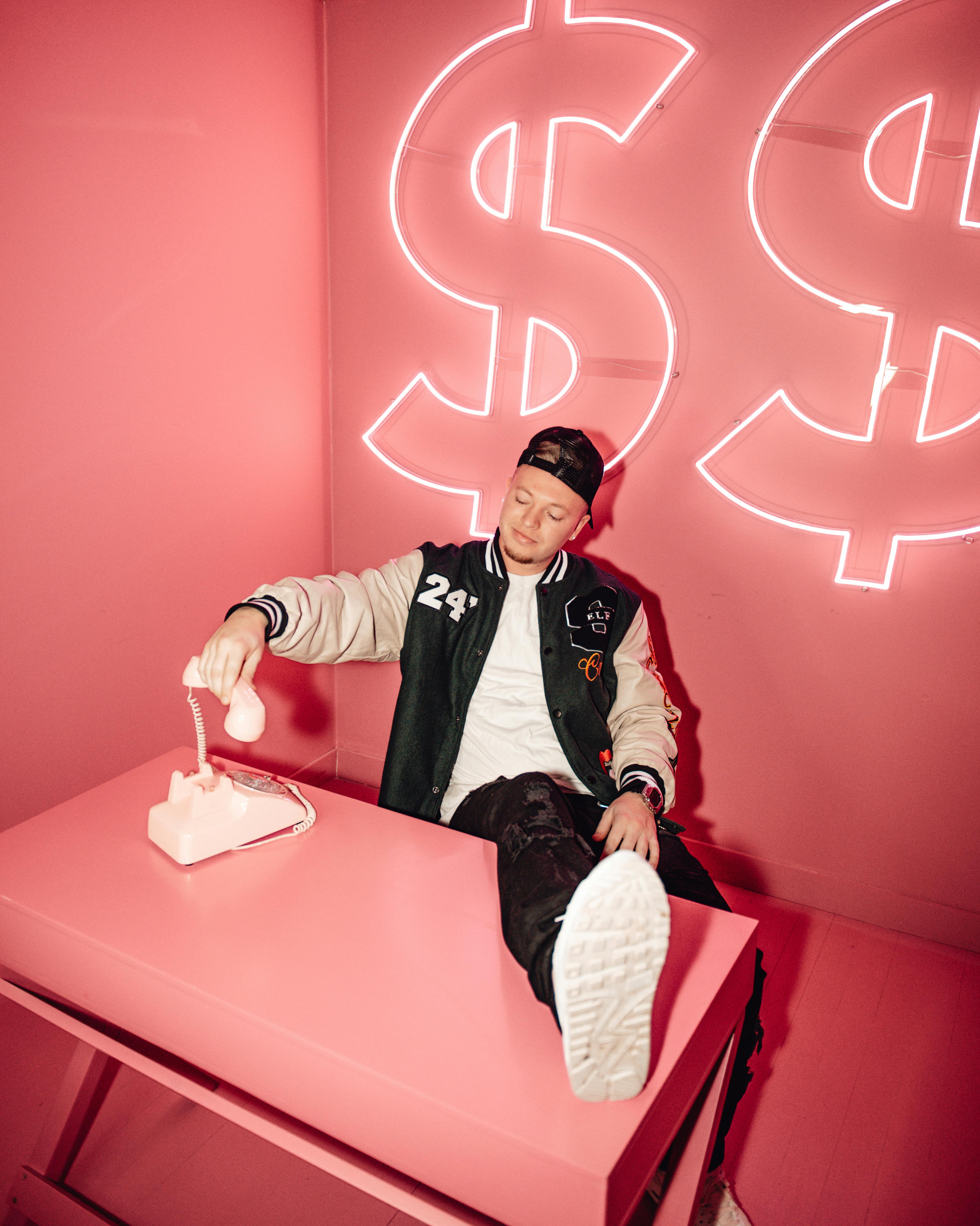 A stylish man posing in a quirky pink room, holding a vintage telephone.