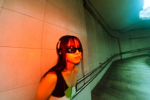 Young Woman Wearing Sunglasses and Headphones Standing in a Tunnel 
