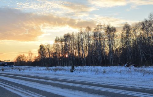 Free Beautiful winter sunset behind a snowy forest with a clear road leading into the horizon. Stock Photo