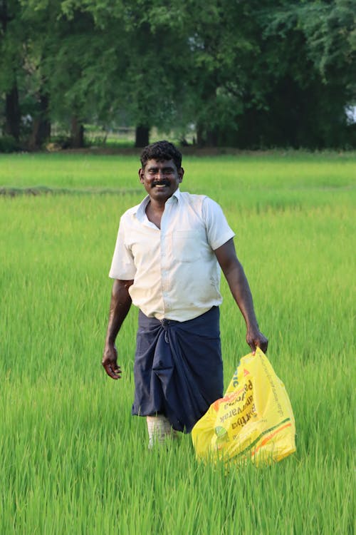 Smiling Man Standing in a Green Field with a Yellow Bag