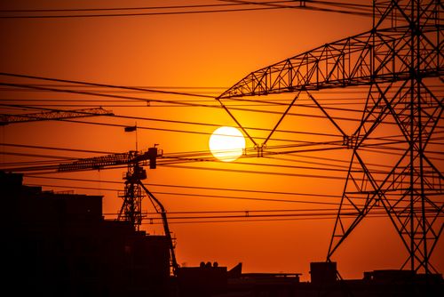 Free Dramatic sunset over Dubai with silhouetted pylons and cranes against an orange sky. Stock Photo