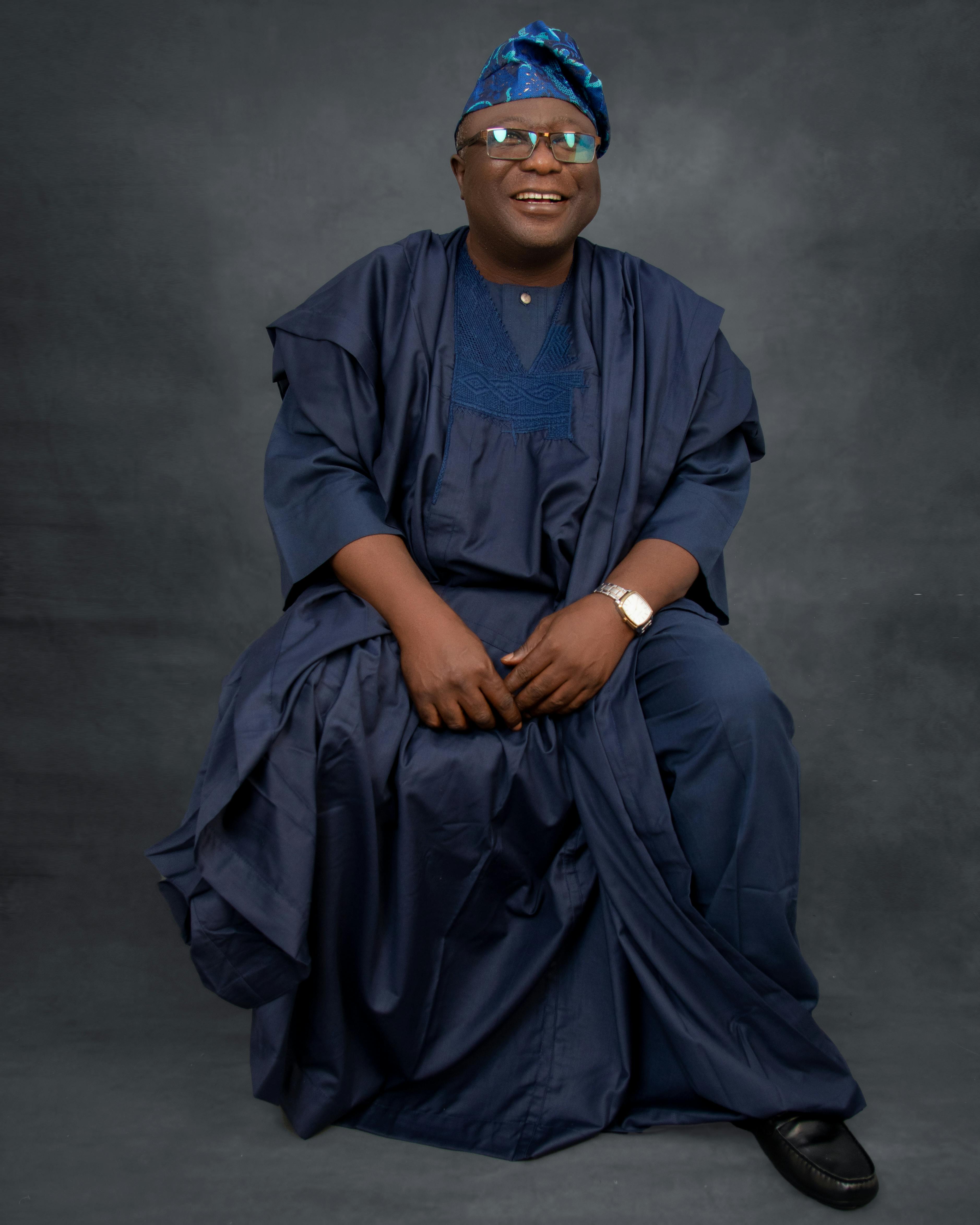 Smiling man in colorful traditional attire, seated in a studio setting.