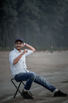 Man in casual attire sitting on a beach chair by the forest edge.