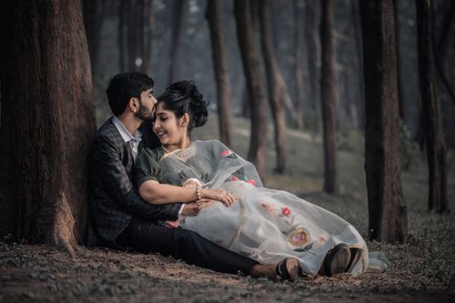 Free A couple sits affectionately under tree trunks in a serene forest, sharing a romantic moment. Stock Photo