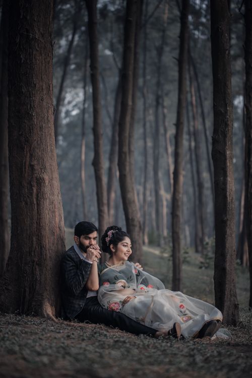 Free A couple sitting against a tree in a beautiful forest, enjoying a tranquil moment. Ideal for love and nature themes. Stock Photo