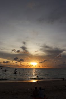 A tranquil beach scene at sunset with silhouetted figures enjoying the ocean view.
